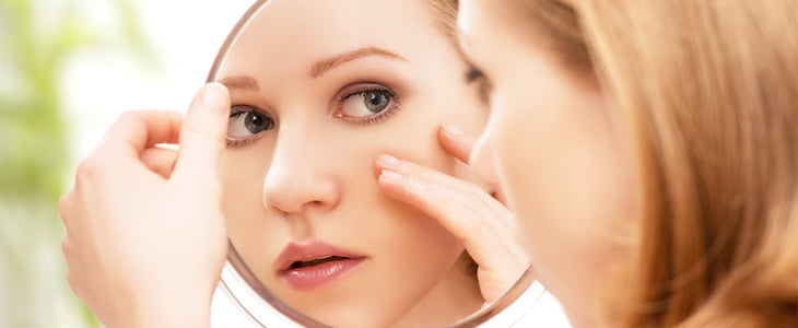 woman inspecting skin in mirror