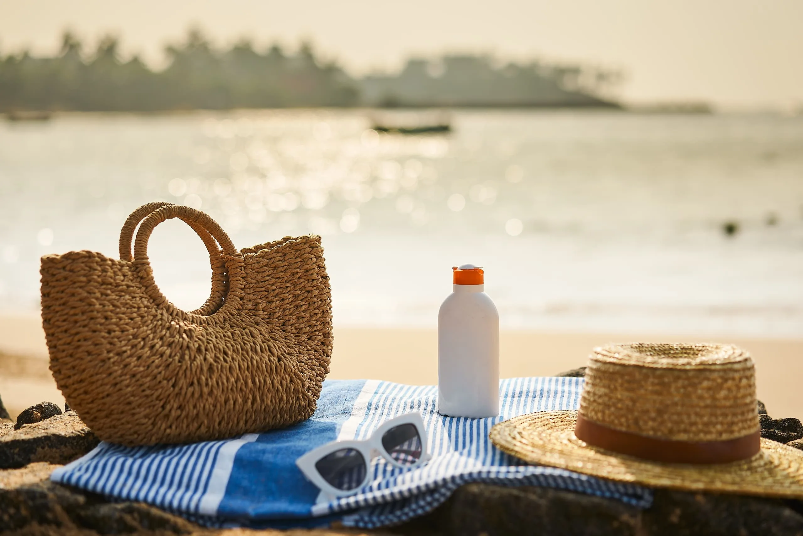 sunscreen on blanket next to bag, sunglasses and beach