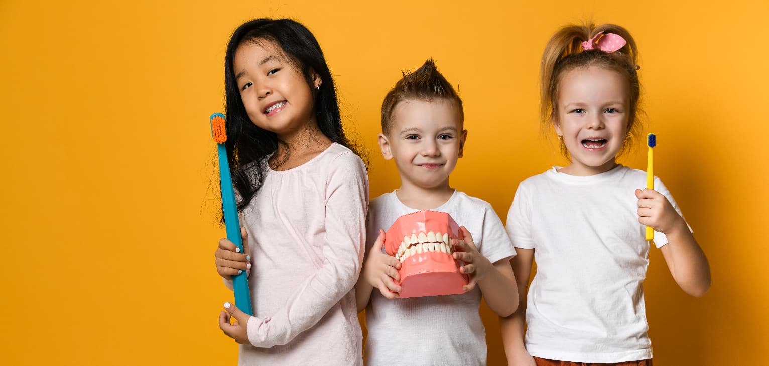 3 children stood together holding toothbrushes and fake teeth