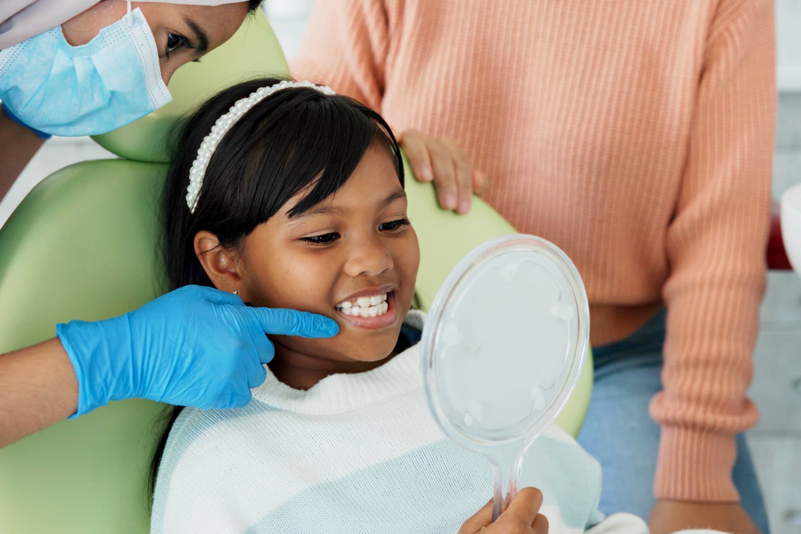 young girl sat in dentist chair with dentist pointing at teeth