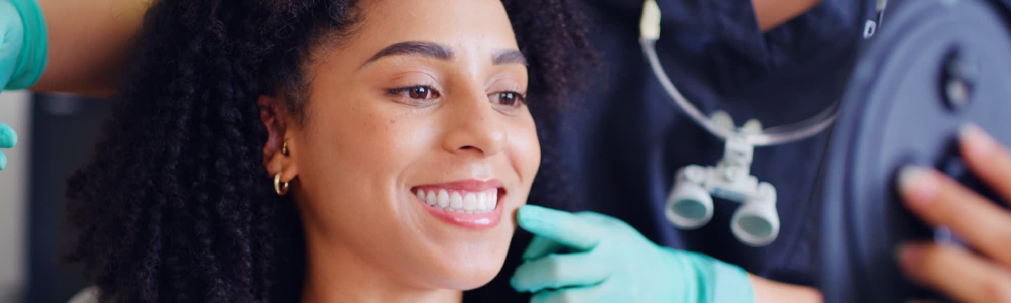 Smiling dental patient looking in a mirror while a dentist reviews treatment results during a cosmetic dentistry consultation appointment