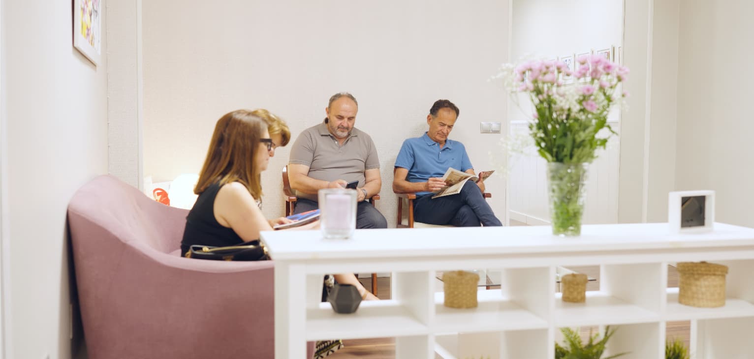 Patients waiting in a bright, modern dental practice reception, with some reading and others using their phones, illustrating the demand for dental appointments in a calm and welcoming waiting area.